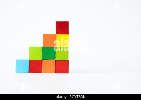 Cubes en bois aux couleurs vives disposés de manière créative en marches ou en escaliers sur un fond blanc, symbolisant la croissance, l'éducation et l'apprentissage Banque D'Images