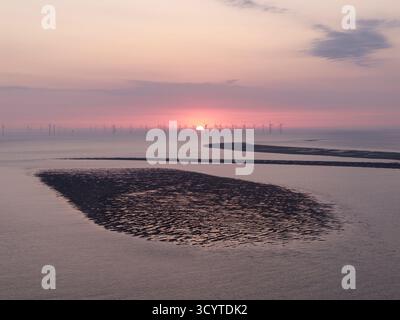 Le soleil se couche derrière les éoliennes dans la baie de Liverpool avec un banc de sable isolé devant eux, vu de New Brighton, Wirral, Angleterre. Le littoral Banque D'Images