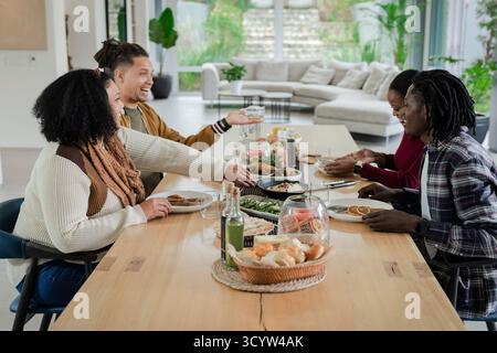Divers amis partageant le repas autour d'une table en bois à la maison avec panier de rouleaux et de salade Banque D'Images