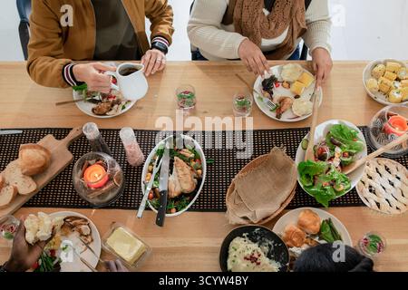 Amis divers partageant un repas commun à la table à manger versant la boisson de la carafe et le rouleau de coupe Banque D'Images