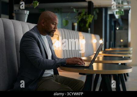 Vue latérale de l'homme d'affaires mature concentré dans Blazer à l'aide d'un ordinateur portable au bureau dans le salon de bureau Banque D'Images