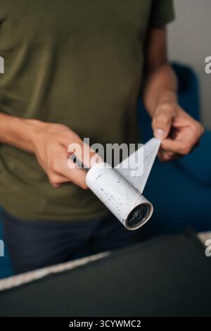 Plan vertical recadré de l'homme pelant la couche usagée de rouleau à peluches collantes, se préparant à nettoyer les vêtements de la poussière, des cheveux et des fibres, assurant des vêtements Banque D'Images