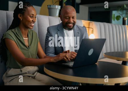 Des hommes d'affaires noirs souriants travaillant sur un ordinateur portable assis au bureau dans le salon Banque D'Images