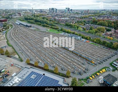Vue aérienne de la cour de manœuvre d'Utrecht avec un train de passagers NS jaune sur des voies vides, entouré par l'horizon de la ville et les infrastructures urbaines à Netherla Banque D'Images