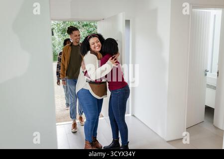 Divers amis serrés à l'entrée de la maison tandis que deux hommes debout sur le sol carrelé près de la porte blanche Banque D'Images