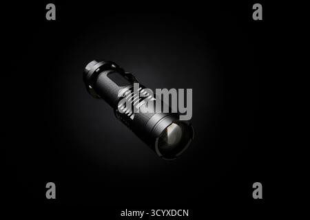 Image de produit professionnelle d'une lampe de poche tactique compacte avec réflexion claire de lentille. L'objet est centré sur un fond noir avec une lig dramatique Banque D'Images