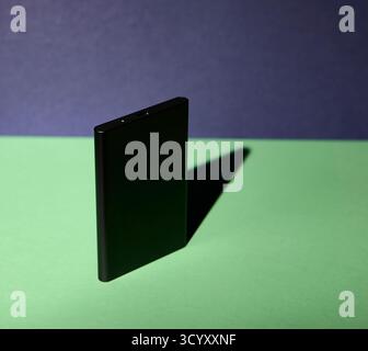 Un disque dur externe noir debout verticalement sur un fond bleu et vert photographié avec un fort éclairage directionnel et un contraste audacieux idéal f Banque D'Images