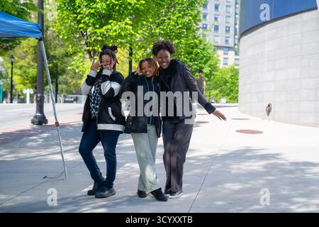 Trois femmes sourient et posent pour une photo sur le trottoir devant l'Aquarium de Géorgie, entourées de verdure par une journée ensoleillée Banque D'Images