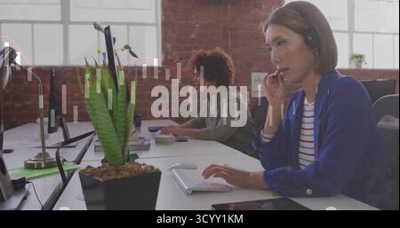 Parlant femme asiatique dans blazer bleu et casque tapant au bureau, avec plante succulente, espace de copie Banque D'Images