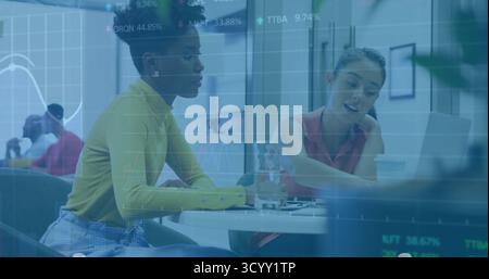 Discuter des collègues penchés sur une table de réunion ronde dans un bureau ouvert, avec ordinateur portable et graphiques Banque D'Images