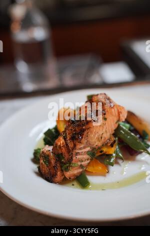 Filet de saumon grillé servi sur une assiette blanche avec des haricots verts frais, des légumes jaunes et des herbes, arrosé d'huile. Un repas gastronomique sain. Banque D'Images