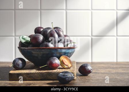 Prunes mûres dans un bol bleu sur fond clair, gros plan Banque D'Images