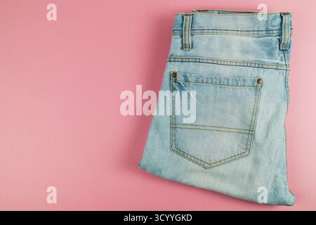 Une paire de jeans en denim bleu clair est soigneusement pliée et placée sur un fond rose doux, mettant en valeur un style décontracté parfait pour un usage quotidien. Banque D'Images