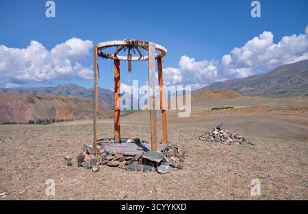 Construction religieuse en bois dans les montagnes de l'Altaï. Fait de poteaux et de pierres en bois. En arrière-plan chaîne de montagnes Kurai sous ciel bleu et nuages. Banque D'Images