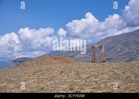 Construction religieuse en bois dans les montagnes de l'Altaï. Fait de poteaux et de pierres en bois. En arrière-plan chaîne de montagnes Kurai sous ciel bleu et nuages. Banque D'Images