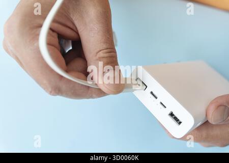 Gros plan d'une main connectant un câble USB à une banque d'alimentation blanche sur fond bleu Banque D'Images