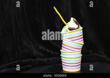 Tasse rayée colorée avec crème glacée au chocolat crémeux et cuillère jaune sur un fond texturé foncé Banque D'Images