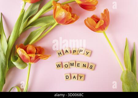 8 mars, carte postale. Affiche textuelle Happy Women's Day avec tulipes orange sur fond rose. Pose plate élégante avec fleurs et texte, carte de vœux Banque D'Images
