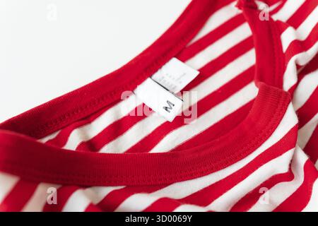 Gros plan d'une chemise rayée rouge et blanche avec une étiquette de taille M. Tissu en coton doux, coutures soignées, coupe confortable Banque D'Images