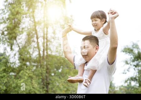 Portrait de famille asiatique en plein air. Père Piggyback fille au parc vert Banque D'Images