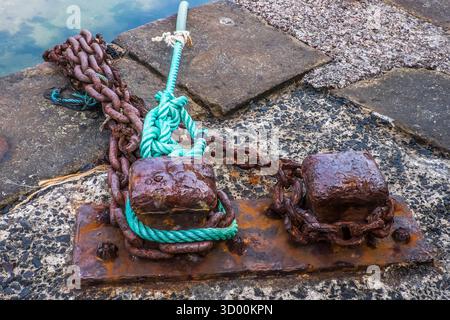 Chaînes d'amarrage rouillées et bornes avec corde verte sur un mur du port Banque D'Images