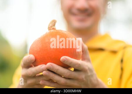 Gros plan de citrouille dans de fortes mains masculines, fermier souriant derrière. Récolte d'automne, légumes frais, alimentation saine, mode de vie naturel, agriculture rurale. Banque D'Images