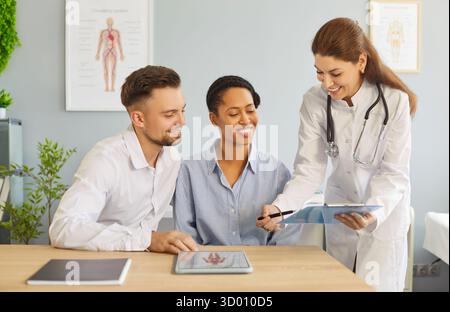 Consultation heureuse en clinique, médecin reproductologue féminin expliquant le résultat du test, aidant le couple Banque D'Images
