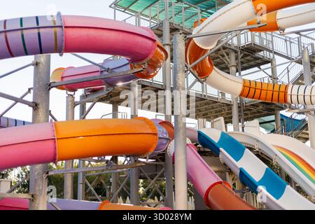 Toboggans aquatiques aux couleurs vives tournent et tournent dans un parc d'attractions animé. Les visiteurs se rassemblent à la base, désireux de profiter de la balade palpitante sur un su chaud Banque D'Images