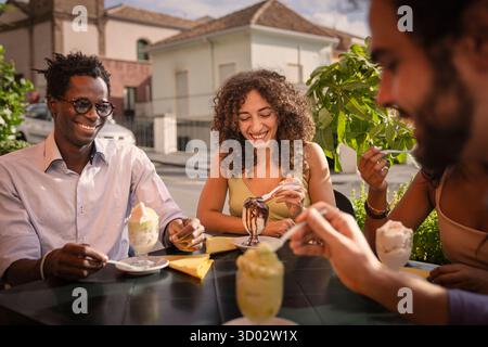 Un groupe multiethnique joyeux de trois jeunes amis riant et parlant tout en mangeant du granita rafraîchissant, un dessert sicilien traditionnel, ensemble à Banque D'Images