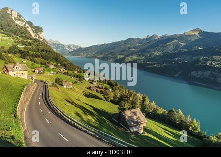 Une route serpente à travers le paysage alpin pittoresque au-dessus du lac Walensee près du village d'Amden dans le canton de Gall, en Suisse. Les collines verdoyantes et les prairies avec des maisons dispersées améliorent la beauté du paysage. Le lac turquoise est sur Banque D'Images