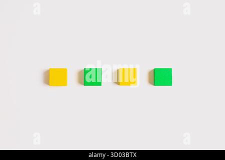 Quatre petits cubes en bois, alternant entre jaune et vert, disposés en ligne horizontale nette sur un fond blanc propre. Banque D'Images