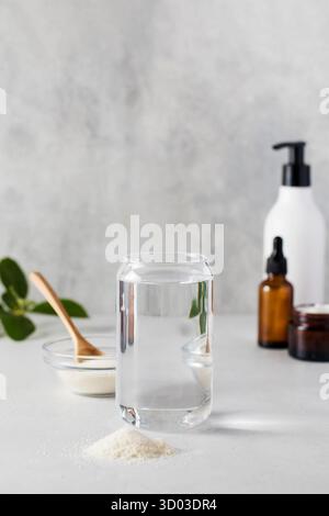 Un verre d'eau, une lame de poudre de collagène et des cosmétiques de soin sur fond gris. Le concept de procédures anti-âge, suppléments nutritionnels pour la santé. Banque D'Images