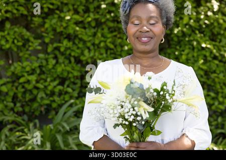 Femme senior tenant un bouquet de fleurs, souriant paisiblement dans le jardin. Jardinage, nature, floraison, loisirs, bonheur, extérieur || autorisation du modèle Banque D'Images