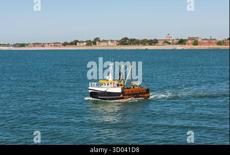 Petit bateau de pêche commerciale bateau chalutier naviguant vers la mer par une journée claire dans l'eau calme avec fond de ciel bleu Banque D'Images