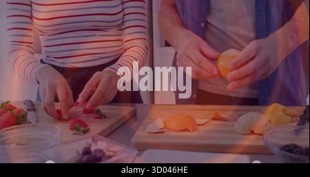 Trancher les fraises et éplucher l'orange, deux amis debout au comptoir en bois avec des bols de fruits Banque D'Images