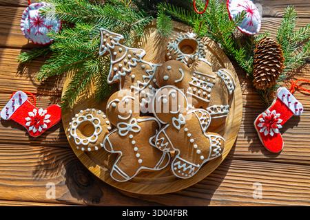 Biscuits festifs au pain d'épices avec décor de vacances. Biscuits en pain d'épices sur le thème de Noël avec glaçage sur une assiette en bois, entourés de branches de pin et Banque D'Images