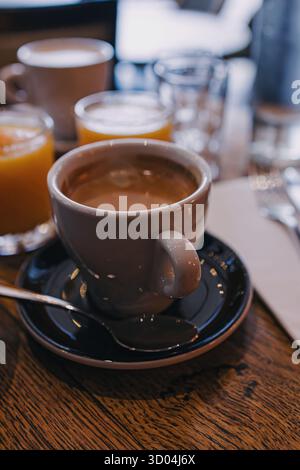 Une scène chaleureuse et accueillante avec une tasse de café sur une table en bois, accompagnée de verres de jus d’orange. Banque D'Images