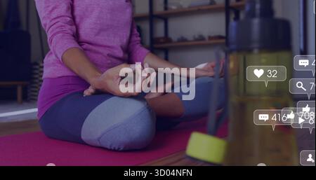 Femme méditante portant des vêtements violets sur tapis de yoga à la maison, avec bouteille d'eau kettlebell icônes sociales Banque D'Images