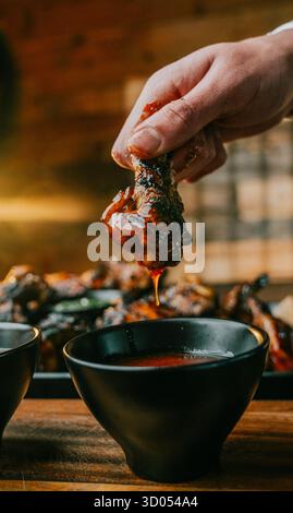 Une personne trempe un morceau de poulet dans une sauce. La sauce est rouge et il est une sauce Banque D'Images