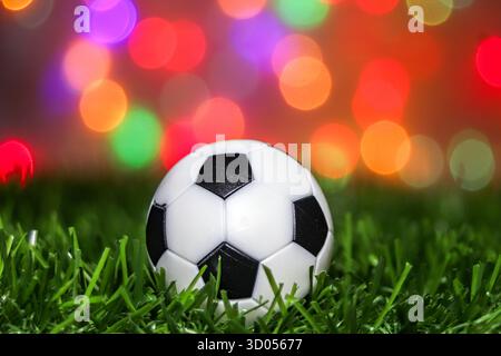 Football sur gazon artificiel vert la nuit contre le bokeh festif et les lumières du stade. Idéal pour les tournois mondiaux et les médias de championnat. Banque D'Images