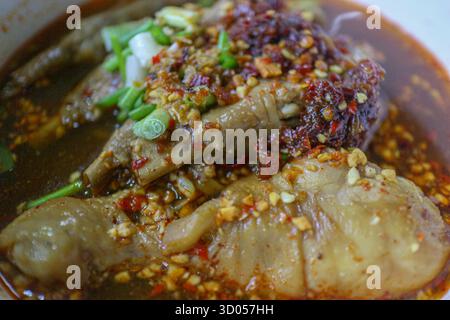 Détail zoomé des pieds de poulet et des pilons dans une soupe épicée et riche aux nouilles thaïlandaises (Guay Teow Gai). Authentique cuisine asiatique réconfortante et texture salée. Banque D'Images