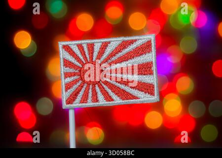 Drapeau japonais du soleil levant contre des lumières bokeh colorées. Culture asiatique, histoire japonaise, symbole traditionnel et médias festifs. Banque D'Images