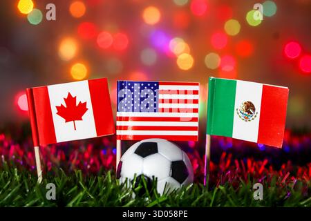 Football avec des drapeaux du Canada, des États-Unis et du Mexique sur l'herbe contre le bokeh festif. Événement mondial majeur, hôtes nord-américains et célébrations sportives. Banque D'Images