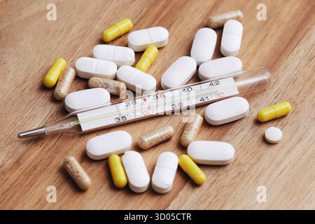 Médicaments et thermomètre sur table en bois. Concept de traitement de la fièvre et de la maladie. Capsules de pilules et fond de soins médicaux. Banque D'Images