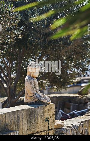 Bouddha en pierre altérée assis dans un jardin calme, feuilles et bokeh, lumière chaude du soleil et ombres douces, humeur spirituelle tranquille Banque D'Images