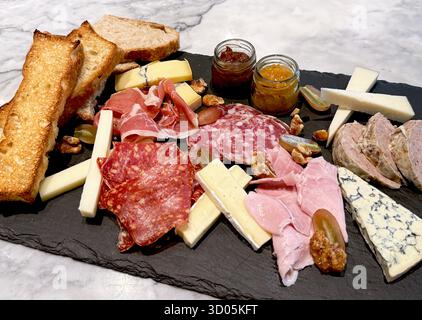 Plateau de charcuterie gourmet avec assortiment de charcuteries, fromages, pain grillé, noix, raisins, et confitures de fruits. Banque D'Images