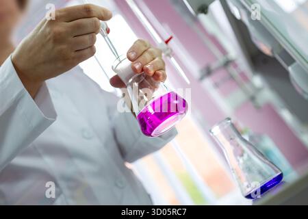 Gros plan d'un scientifique pipettant pendant un titrage avec indicateur rose dans un flacon, parfait pour la chimie, l'éducation, l'industrie pharmaceutique, la biotechnologie et la R & D. Banque D'Images