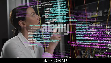 Tenant le stylo sur les lèvres, portant une chemise à col inspectant le code dans le centre de données avec des câbles, copiez l'espace Banque D'Images