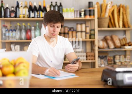 Jeune vendeur masculin prenant des notes dans les documents Banque D'Images