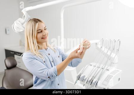 Patient souriant regardant un moule dentaire dans le cabinet d'un dentiste, apprenant sur l'hygiène dentaire et les options de traitement Banque D'Images